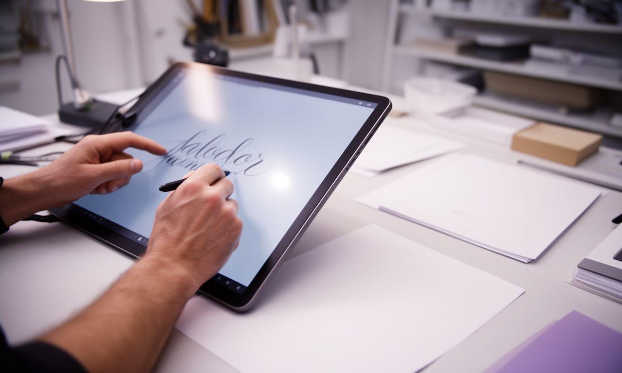 Mains de calígrafa revisando una tableta digital en un estudio luminoso de Madrid con bocetos tipográficos y papel artesanal